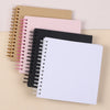 A stack of spiral-bound paper scrapbooks in pink, black, and tan colors.