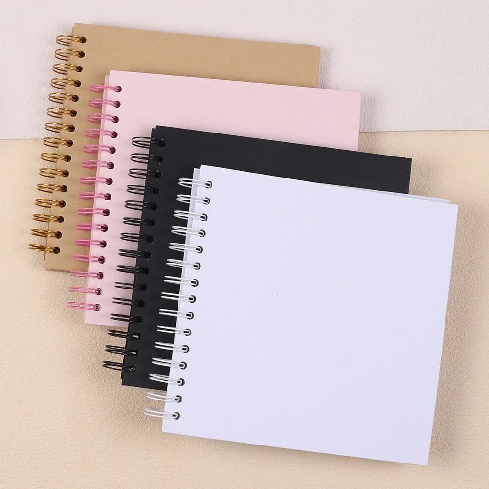 A stack of spiral-bound paper scrapbooks in pink, black, and tan colors.