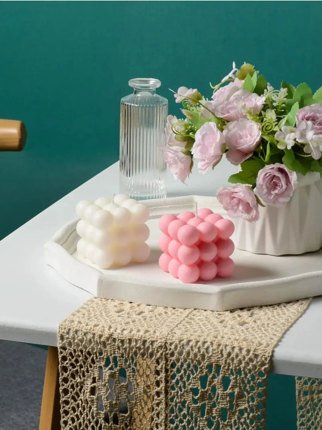 A set of two white and pink cube soy wax candles displayed on a white tray with a glass bottle in a teal background.