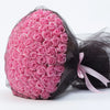 A bouquet of pink silk roses wrapped in sheer black cellophane with a pink ribbon.