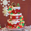 A multi-tiered red and white cake decorated with festive foam ball toppers, including a Christmas tree and a zodiac symbol.