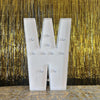 A large white marquee light-up letter W stands against a shimmering gold curtain backdrop.