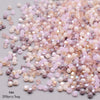 A pile of faceted bicone glass beads in mixed shades of pink, lavender, and cream.