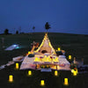 A nighttime outdoor celebration setup featuring a pyramid structure decorated with flowers and illuminated by numerous glowin