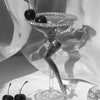 A glass sculpture of a shoe with cherries on the top, set against a white background.