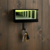 A black rectangular keychain holder with an LED tunnel effect is mounted on dark wood paneling.