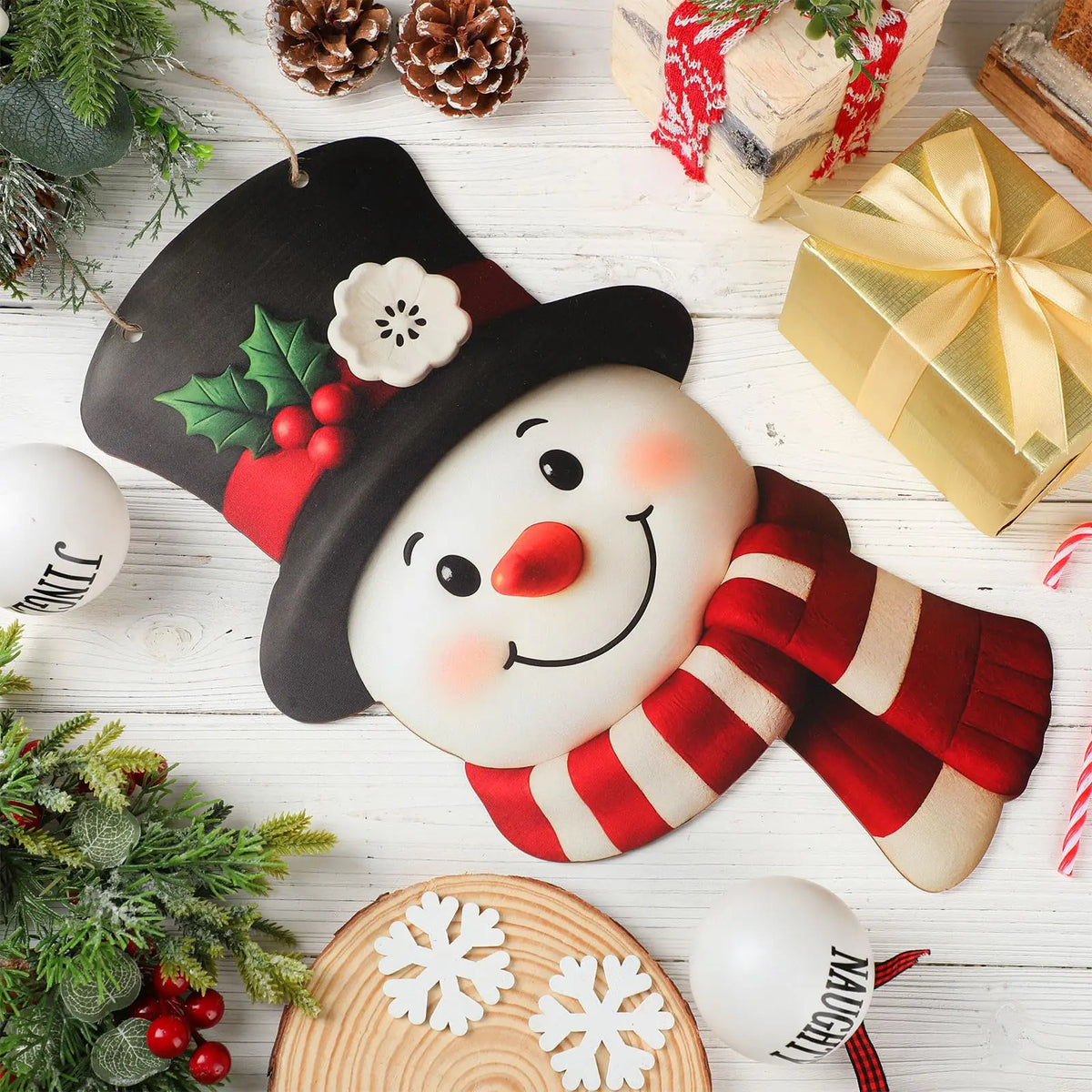 A wooden door wreath shaped like a smiling snowman with rosy cheeks and a striped scarf, set on a white wooden surface.