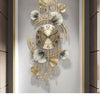 A gold-toned metal wall clock featuring a ginkgo leaf design with Roman numerals, mounted on a light gray wall.