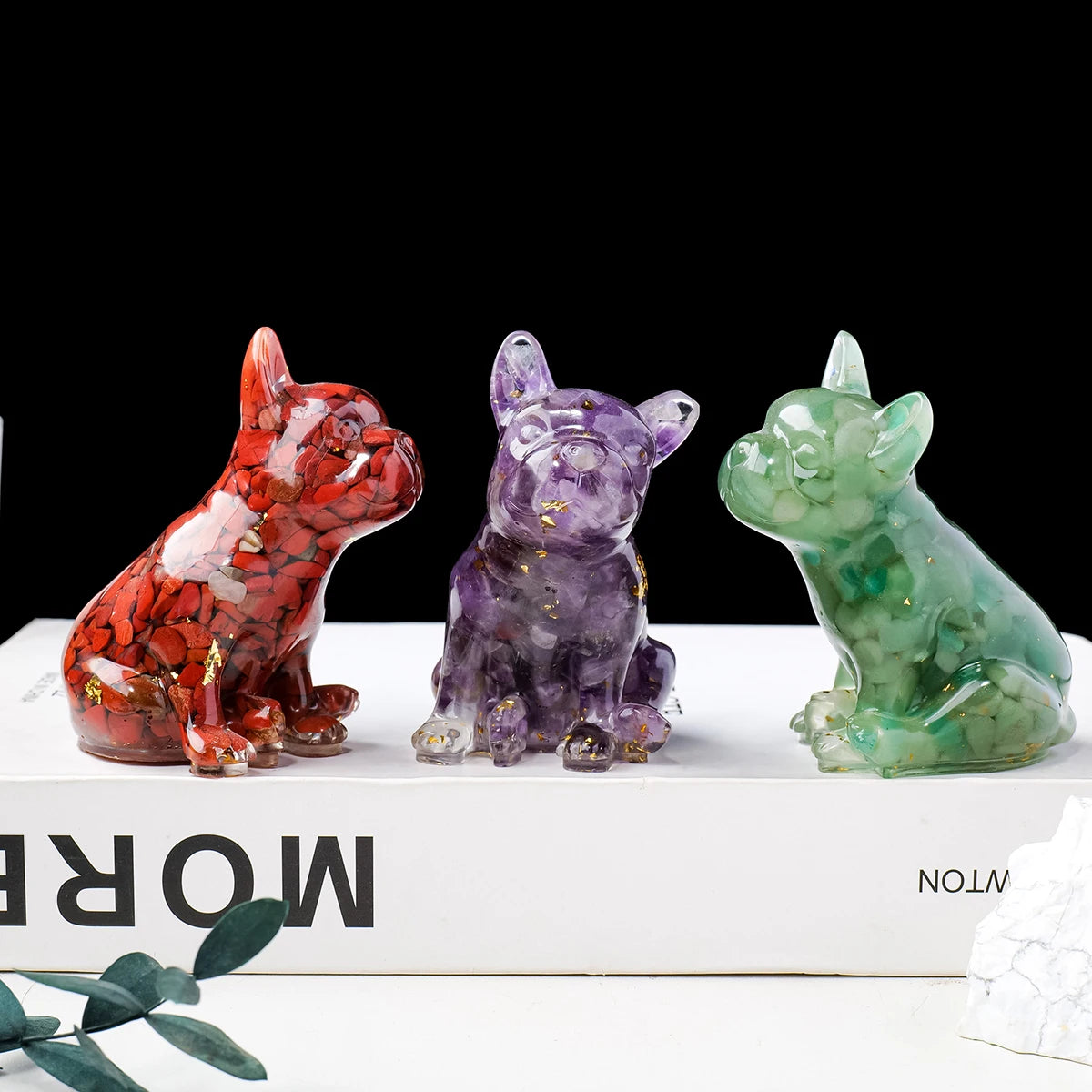 Three natural crystal dog statues in red, purple, and green sitting on a white box.
