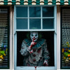 A painted face of a horror carnival clown with green hair and red accents is displayed in a window frame.