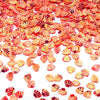A close-up of small, orange and pink sea shell PVC sequins scattered on a white background for nail art and craft decoration.