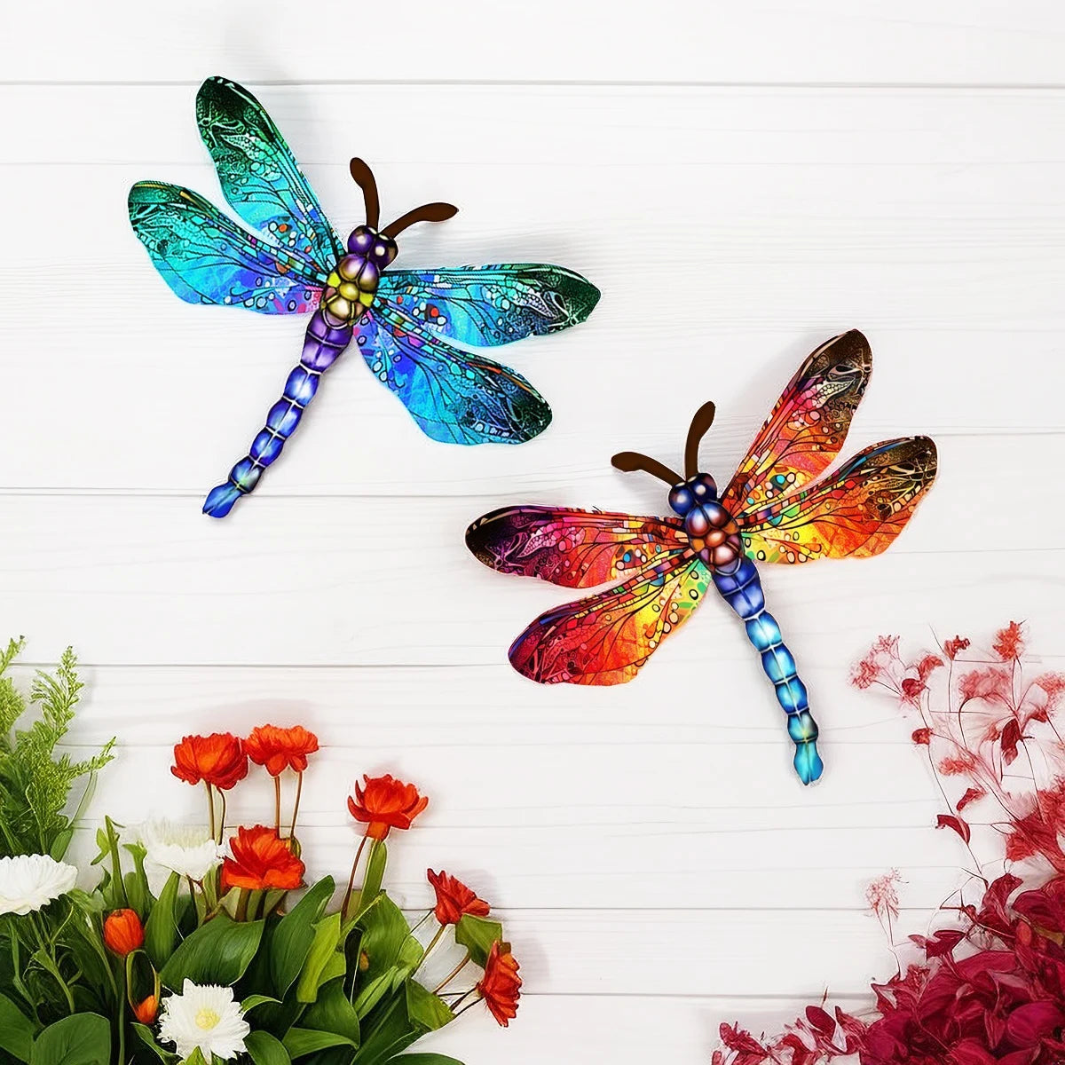 A pair of iridescent dragonfly wall art sculptures featuring vibrant blue and orange wings on a white wooden background.
