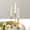 A set of three tall white candles in vintage gold metal holders displayed on a reflective surface.
