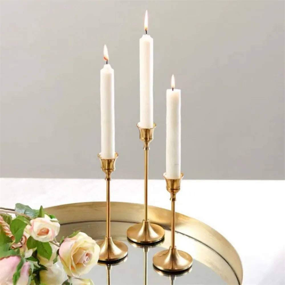 A set of three tall white candles in vintage gold metal holders displayed on a reflective surface.