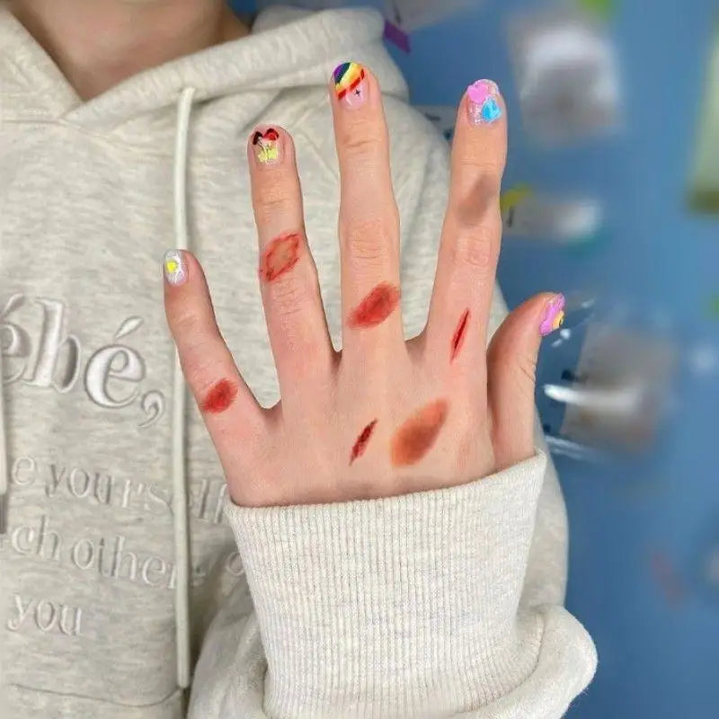 A hand with colorful temporary tattoos and realistic bruises is shown against a light gray hoodie.