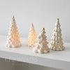 White ceramic glow-in-the-dark mini Christmas tree decor arranged on a white surface.