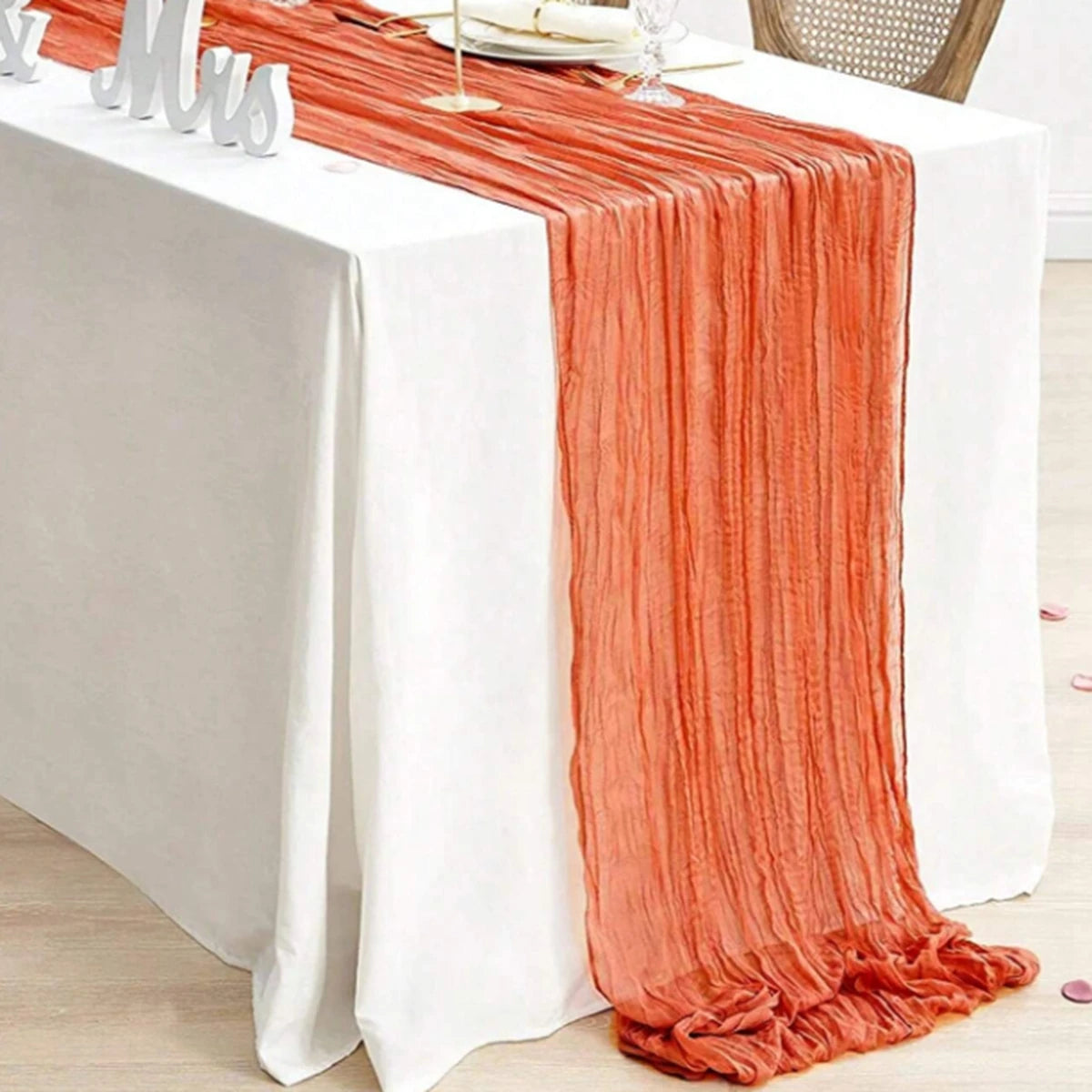 A semi-sheer orange table runner draped on a white tablecloth for an event.