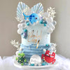 A light blue cake decorated with sea animals, pearl balls, and a silver script birthday message.