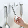 A hand is installing a stainless steel self-adhesive wall hook onto a white surface.