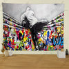 A black and white photograph of a person in a hoodie standing amidst vibrant street graffiti art on a tapestry.