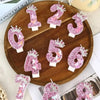 A wooden board displays pink glitter birthday candles shaped like numbers 1 through 8.