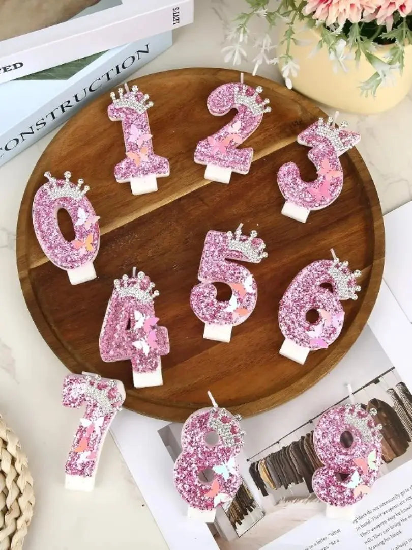 A wooden board displays pink glitter birthday candles shaped like numbers 1 through 8.