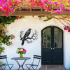 Black raven metal wall art mounted on a white stucco wall under pink flowering vines.