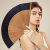 A woman holds an elegant bamboo folding fan with a classic design against a light background.