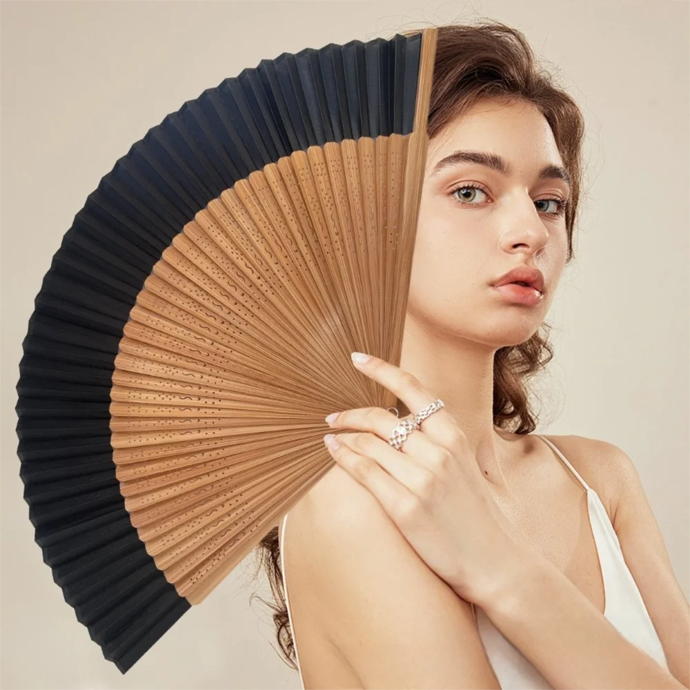 A woman holds an elegant bamboo folding fan with a classic design against a light background.