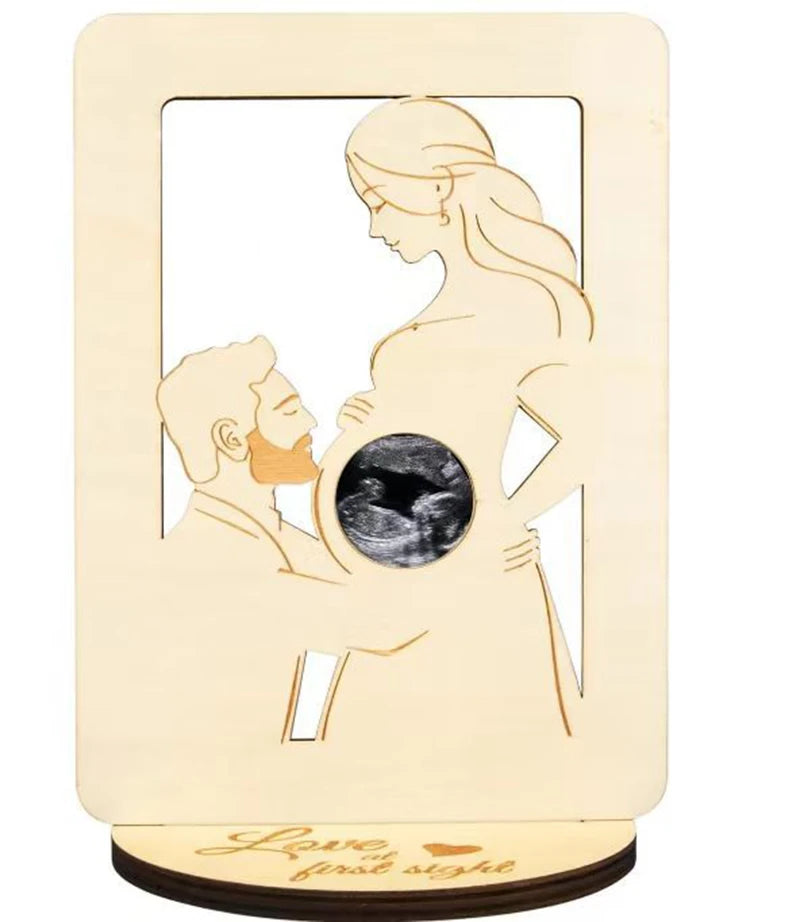 A wooden sign featuring a silhouette of a pregnant woman holding a baby, with the text Love at first sight below.
