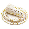 A stack of white and gold polka dot disposable party tableware, including a cup and plates.