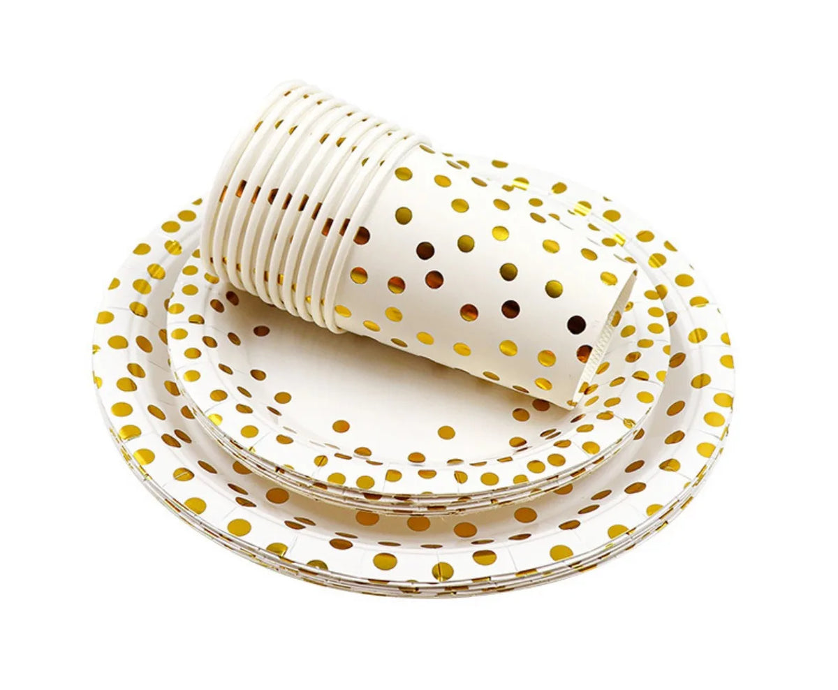 A stack of white and gold polka dot disposable party tableware, including a cup and plates.
