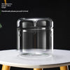 A clear glass decor vase with a rounded top and cylindrical body sits on a white surface.
