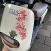 A white motorcycle dashboard ornament featuring pink peach blossoms and the text XDAG and NICE.
