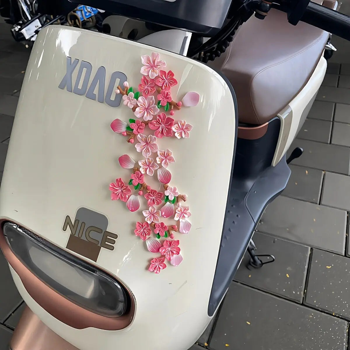 A white motorcycle dashboard ornament featuring pink peach blossoms and the text XDAG and NICE.