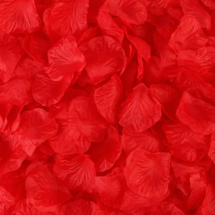 Gros plan de nombreux pétales de roses artificielles rouges et brillants éparpillés sur une surface.