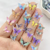 A hand holds a collection of 30 colorful resin butterfly embellishments in various shades of blue, purple, and yellow.
