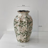 A rustic ceramic milk pitcher with a cracked glaze and pastoral design, featuring green foliage patterns.