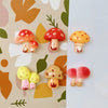 A set of nine colorful, cute decorative mushroom fridge magnets on a patterned background.
