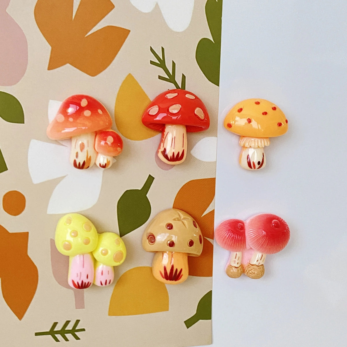 A set of nine colorful, cute decorative mushroom fridge magnets on a patterned background.