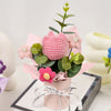A pink handmade crochet tulip bouquet with green leaves displayed in a light pink vase.