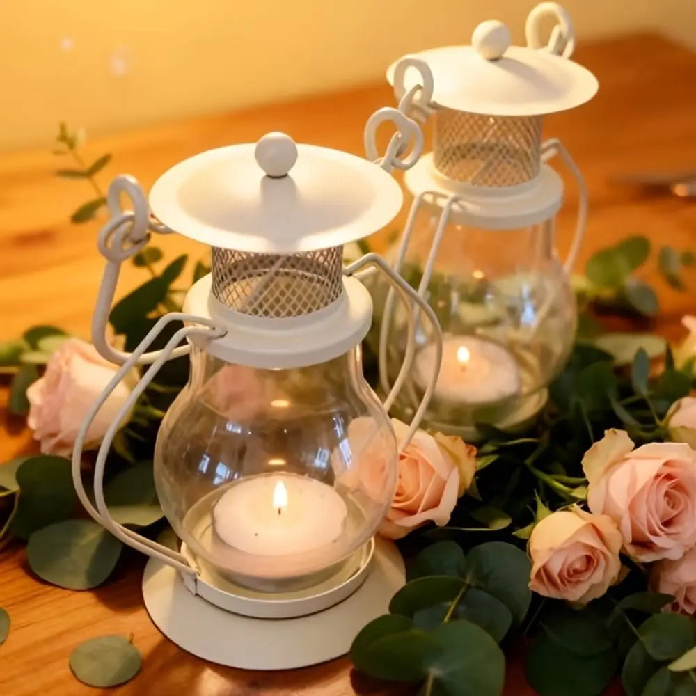 A decorative metal candlestick lantern with a glass globe and a white lid, surrounded by pink roses and green leaves.