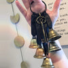 A hand holds a decorative metal wind chime featuring dark leather accents and various sized metal bells.