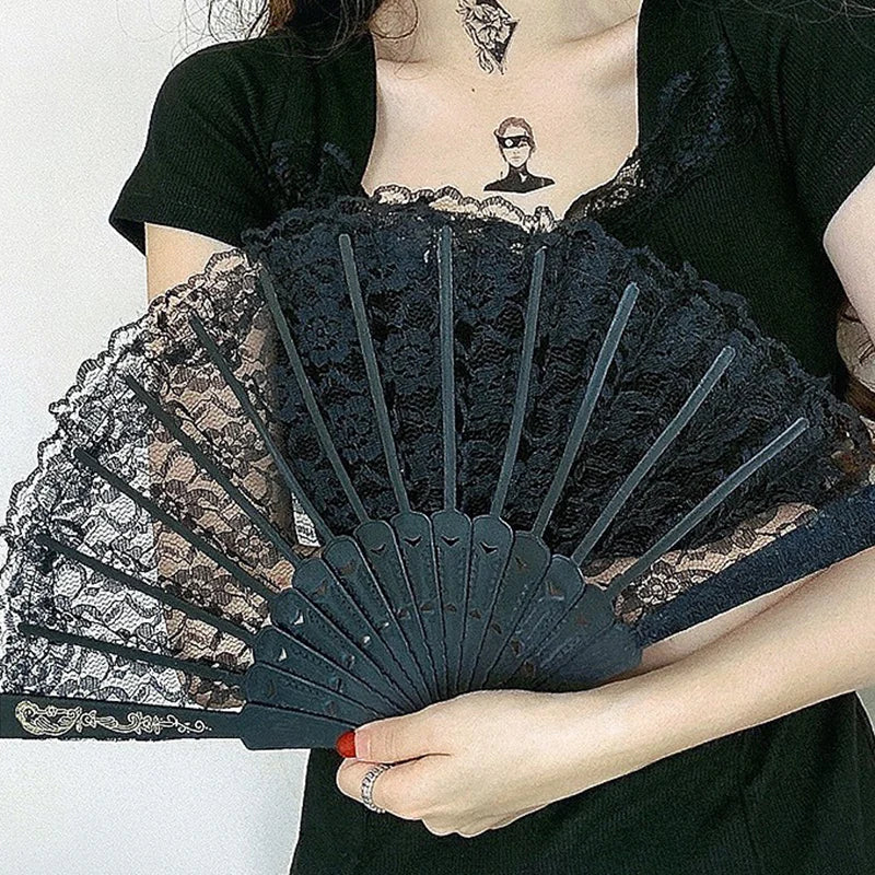 A black lace folding hand fan is held by a person, featuring intricate floral patterns.