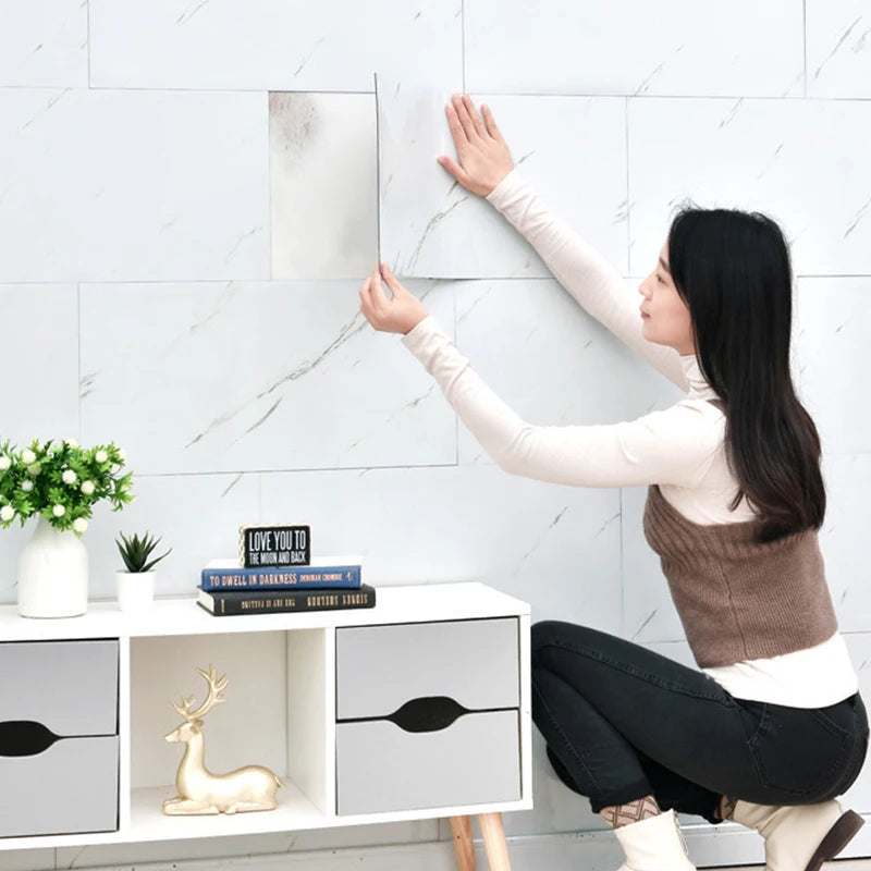 A woman is applying marble wall decals to a white tile surface in a modern setting.