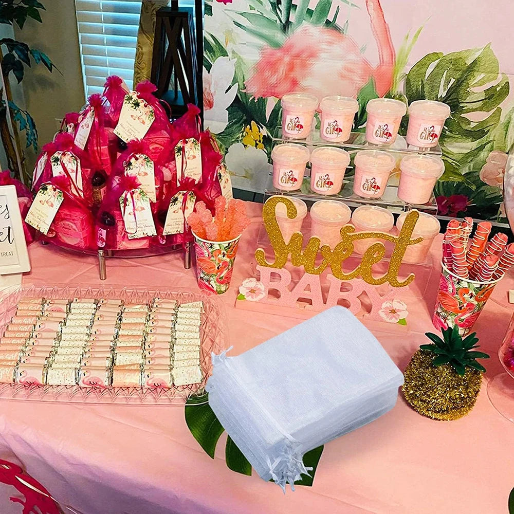 Elegant white and gold drawstring organza bags displayed on a pink table with floral decorations.
