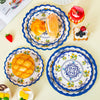 A collection of blue floral disposable paper plates featuring various food items like bread, fruit, and cheese.