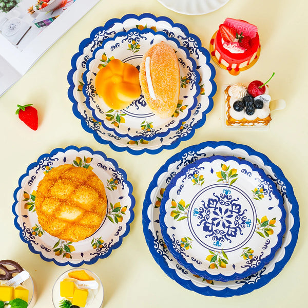 A collection of blue floral disposable paper plates featuring various food items like bread, fruit, and cheese.