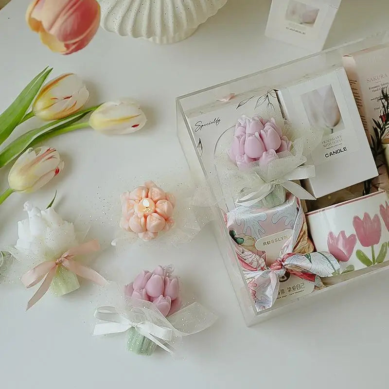 A clear glass box containing a pink tulip candle and other floral elements on a white surface.