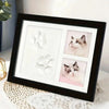 A black photo frame displaying white clay paw print molds and a photograph of a cat.